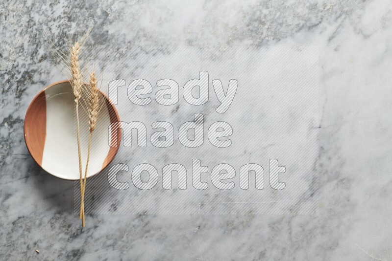 Wheat stalks on multicolored pottery plate on grey marble background