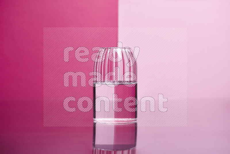 The image features a clear glassware filled with water, set against pink background