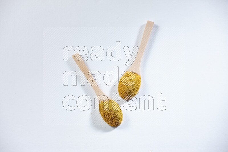 2 wooden spoons full of turmeric powder on white flooring