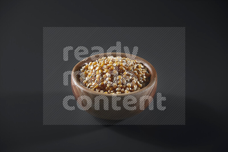 Dry corn kernels in a wooden bowl on grey background