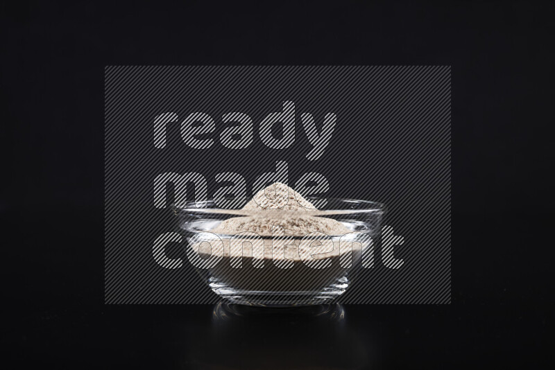 A glass bowl full of onion powder on black background