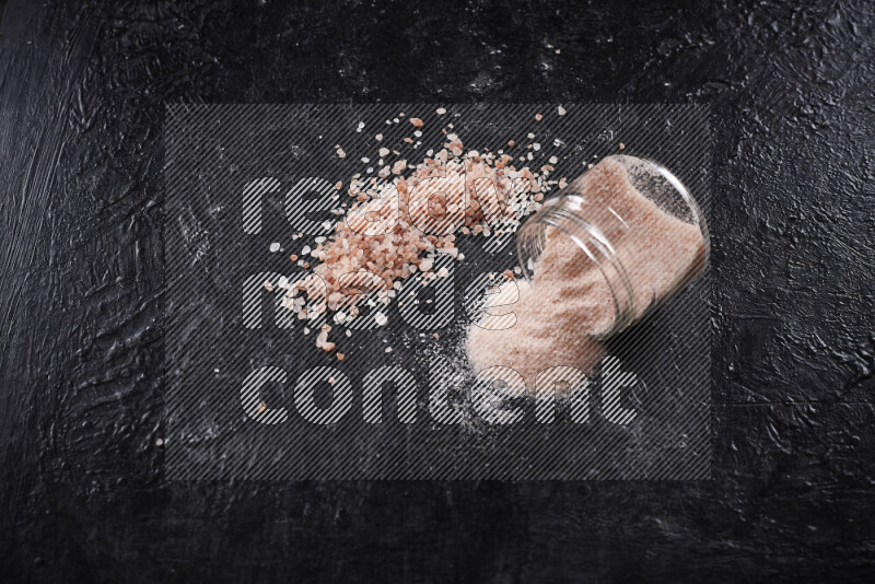 A glass jar full of fine himalayan salt with some himalayan crystals beside it on a black background