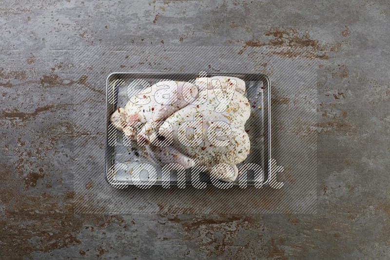 whole Raw chicken on a small oven trey direct on a rustic grey background