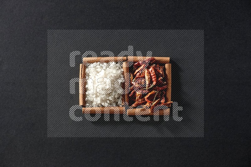 2 squares of cinnamon sticks full of chilis and salt on black flooring