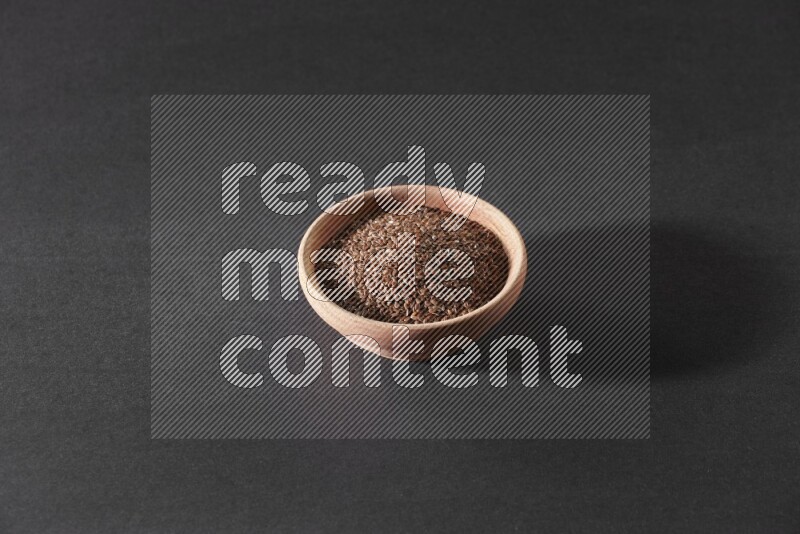 A wooden bowl full of flaxseeds on a black flooring