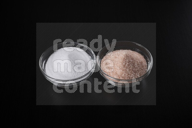 2 glass bowls one is filled with himalayan salt and the other with white salt on black background