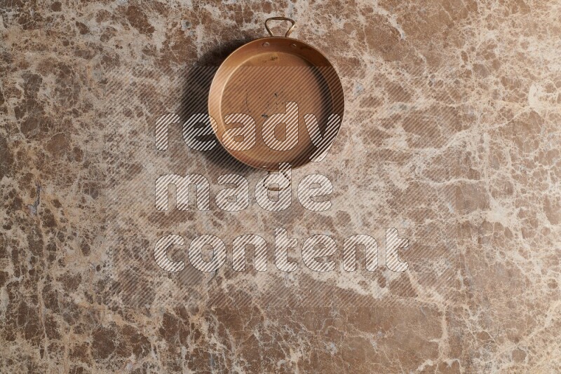 A small copper pan on beige marble background