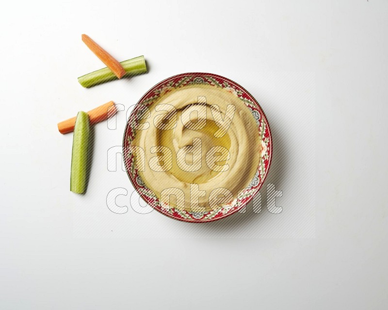 Hummus in a red plate with patterns garnished with olive oil on a white background