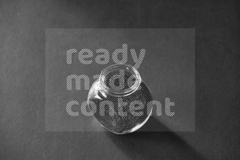 A glass spice jar full of black seeds on black flooring