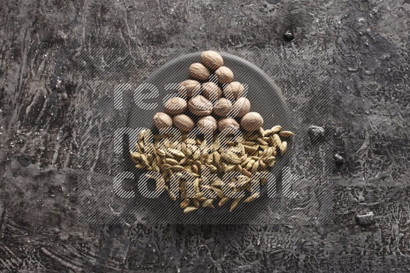 Cardamom and nutmeg on a black plate on textured black background