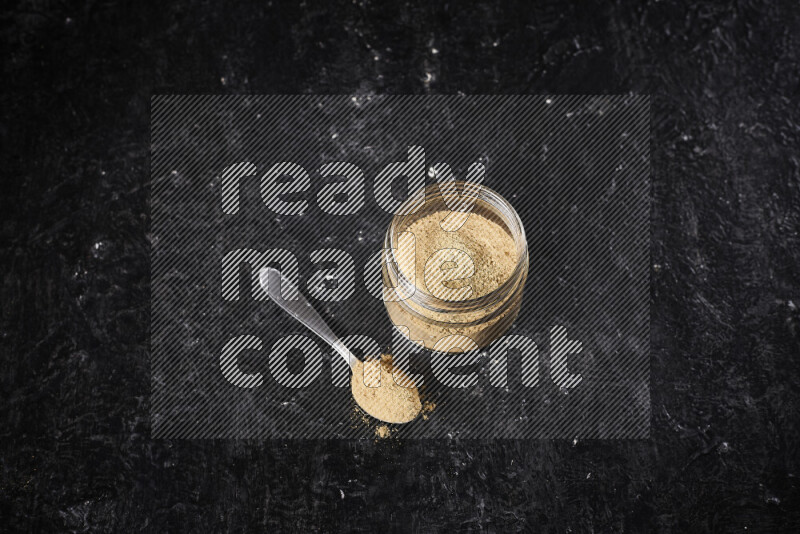 A glass jar full of ground ginger powder on black background