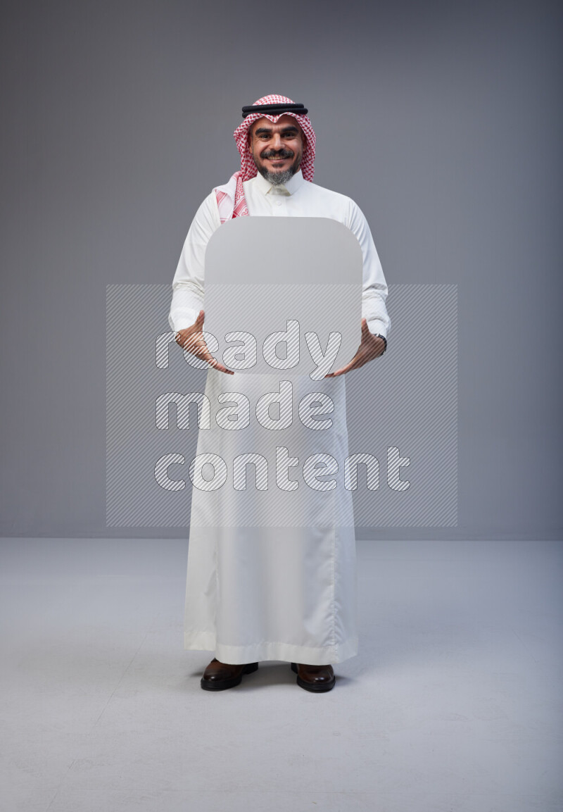 Saudi man Wearing Thob and red Shomag standing holding social media sign on Gray background
