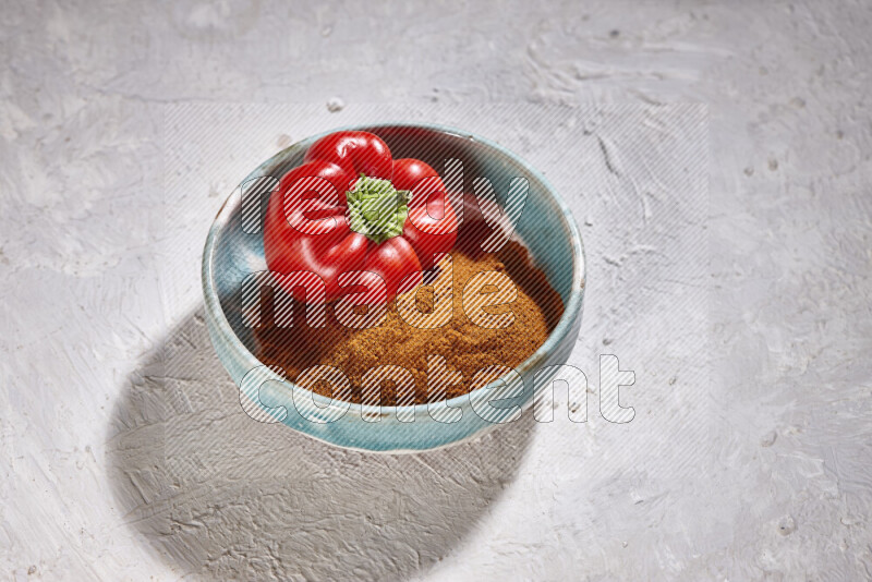 A colored pottery plate full of ground paprika powder and red bell pepper on white background