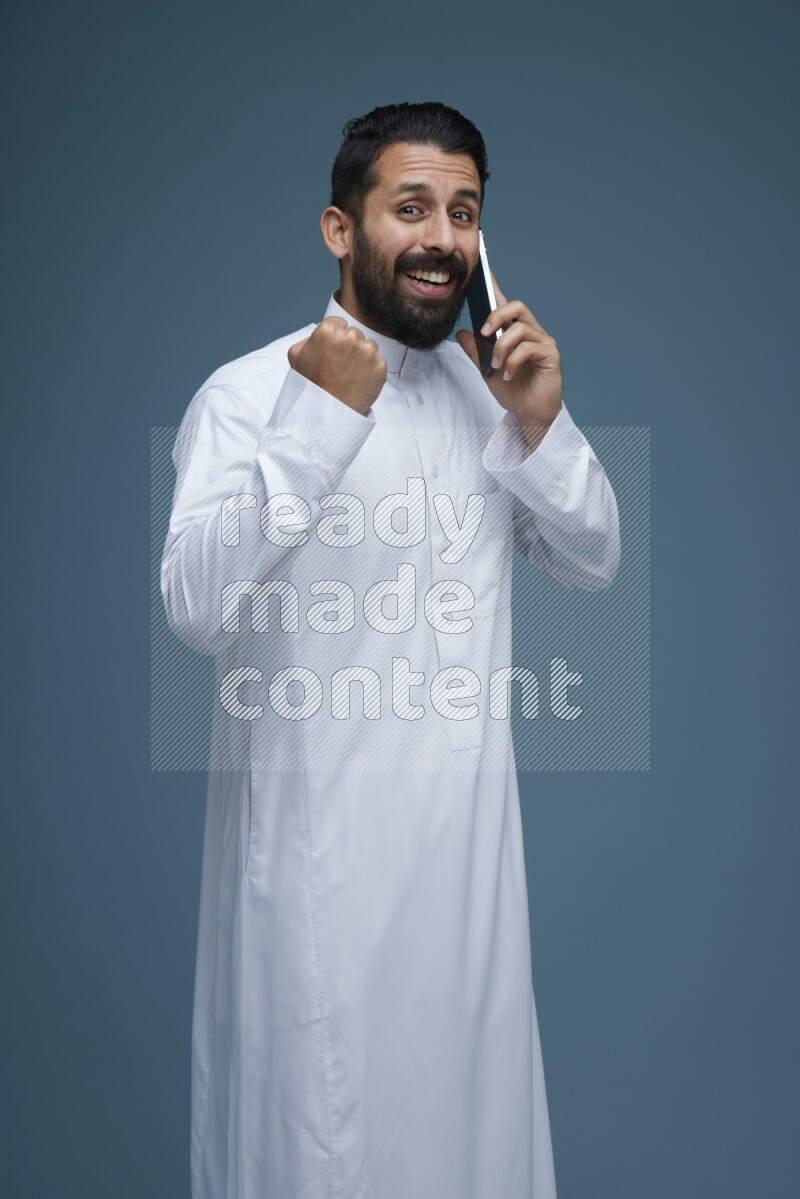 A man having a call on a blue background wearing Saudi Thob