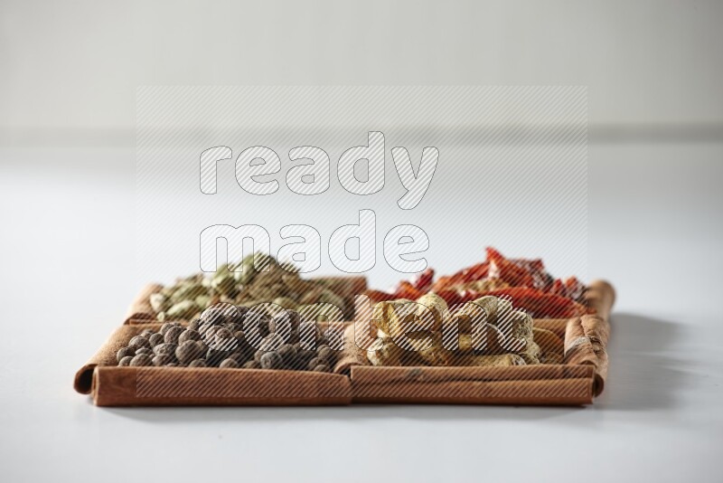 4 squares of cinnamon sticks full of dried red chilis, cardamom, turmeric fingers and allspice on white flooring