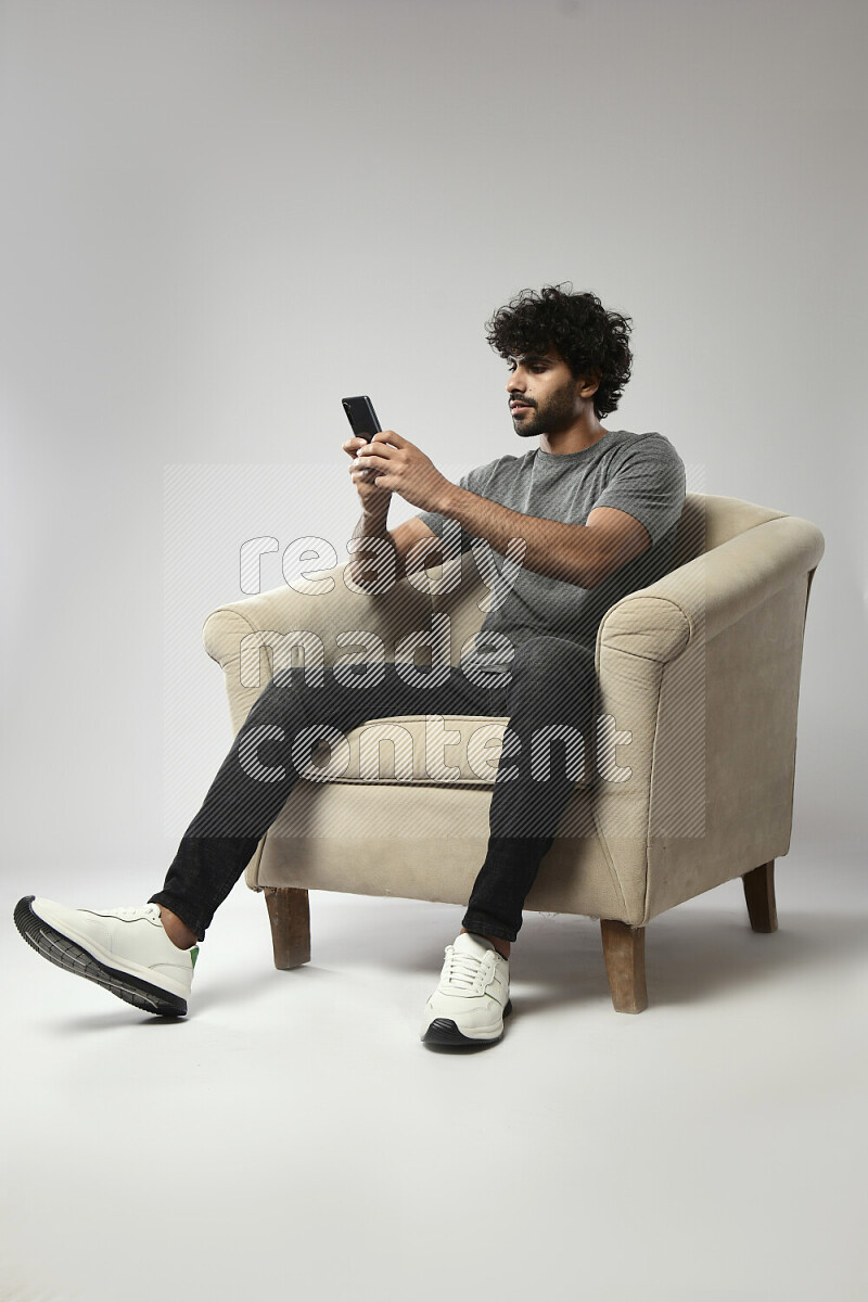 A man wearing casual sitting on a chair texting on the phone on white background