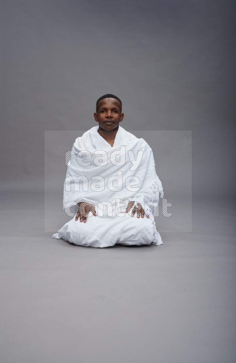 A man wearing Ehram sitting on floor praying on gray background