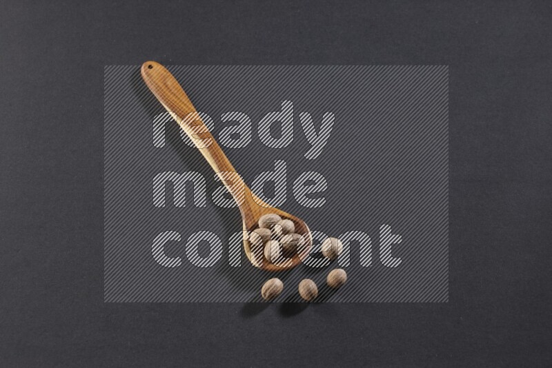 A wooden ladle full of whole nutmeg seeds on a black flooring