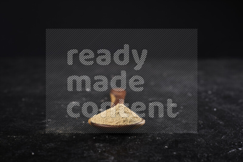 A wooden ladle full of ground ginger powder on black background