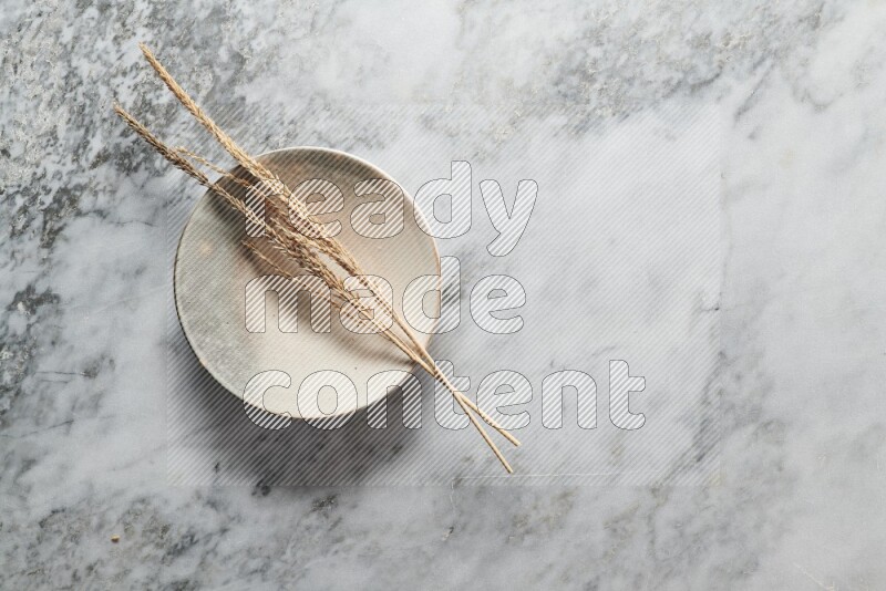 Wheat stalks on multicolored pottery plate on grey marble background