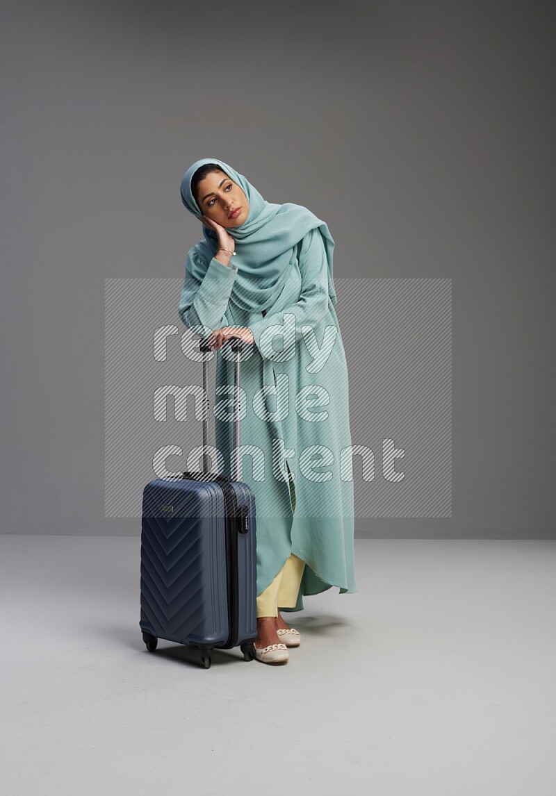 Saudi Woman wearing Abaya standing holding Travel bag on Gray background