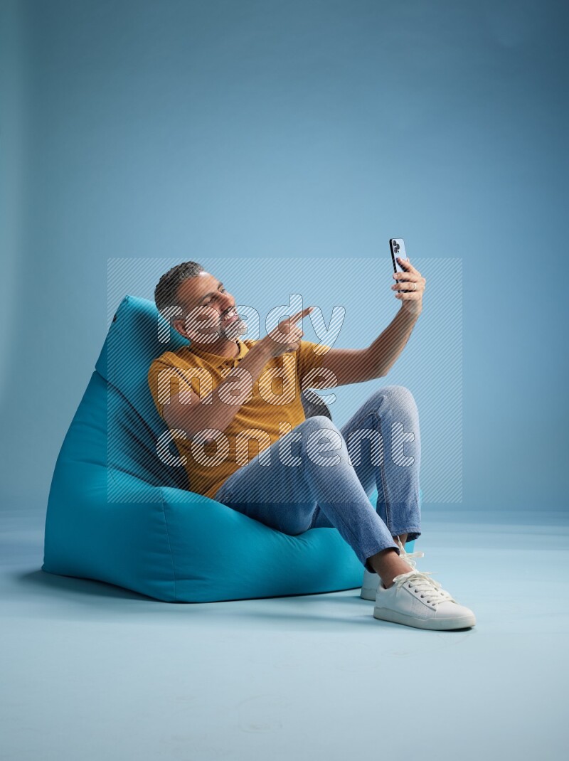 A man sitting on a blue beanbag and taking selfie