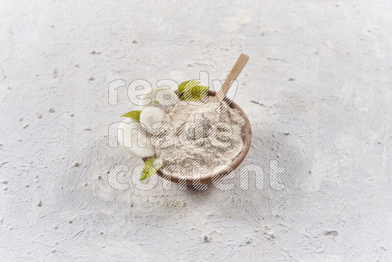 A wooden bowl full of onion powder with a wooden spoon in it with some sliced onions on white background