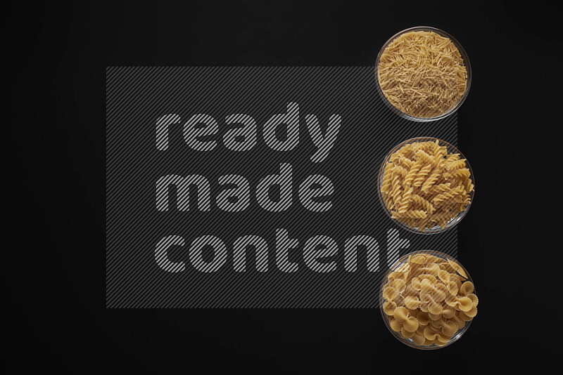 Different pasta types in 3 glass bowls on black background