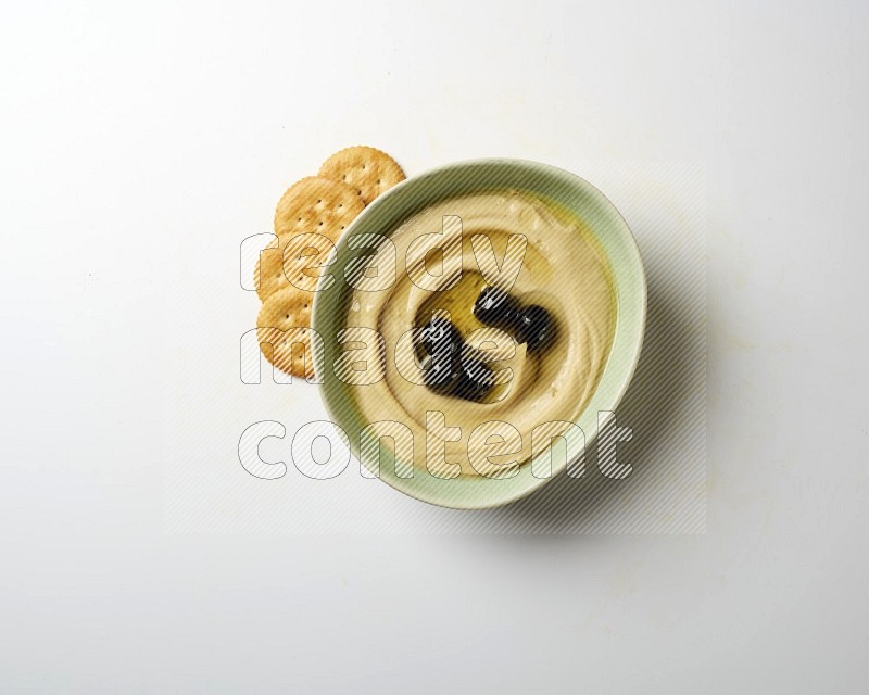 Hummus in a green plate garnished with black olives on a white background