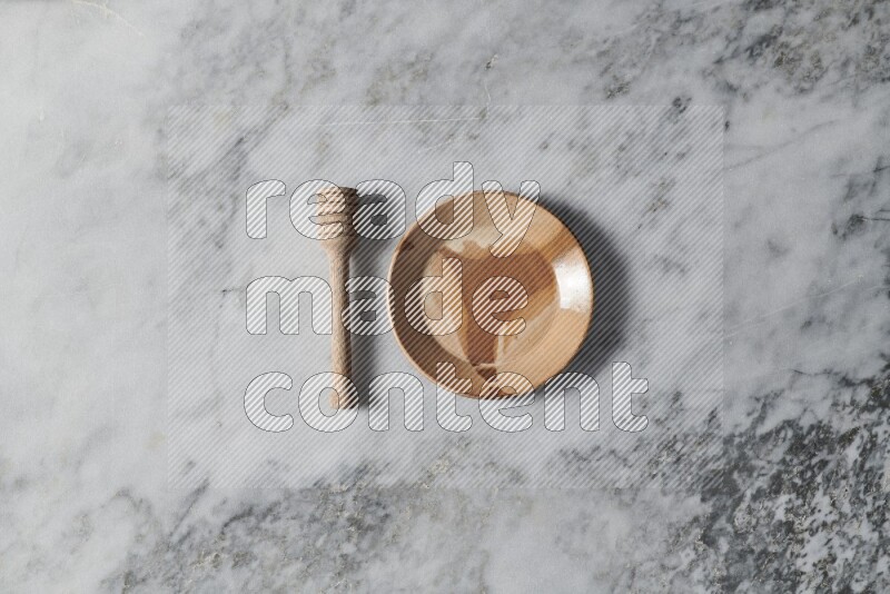 Multicolored pottery plate with wooden honey dipper on the side on grey marble background