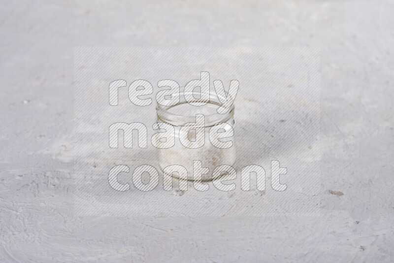 A glass jar full of coarse sea salt crystals on white background