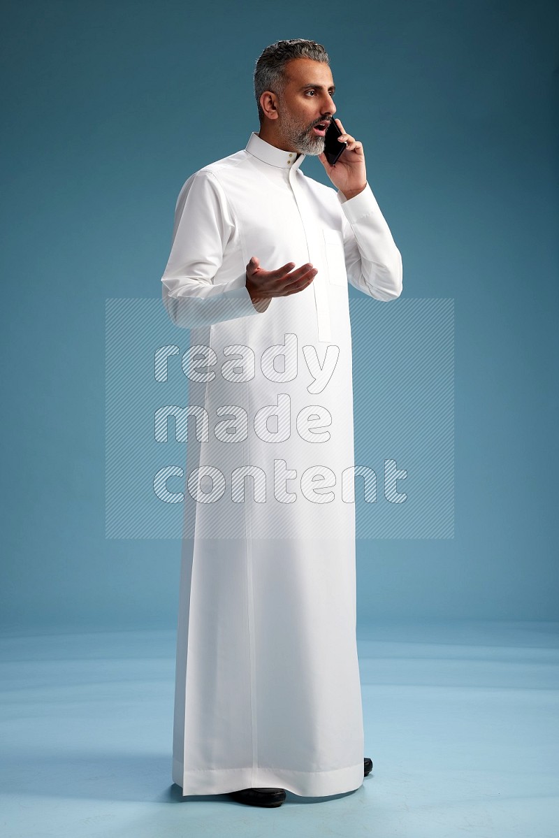 Saudi man wearing thob talking on the phone on blue background