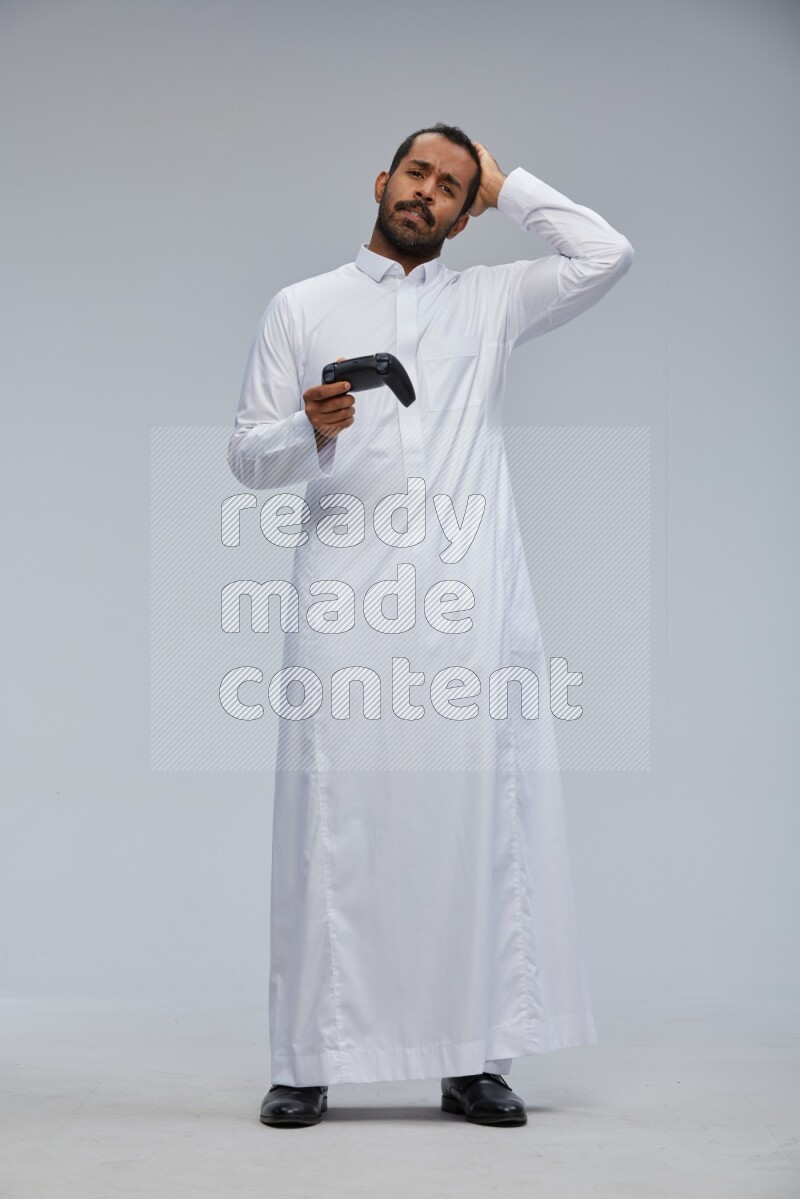 Saudi man Wearing thob standing holding joystick on Gray background