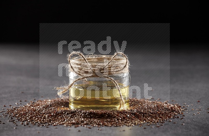 A glass jar full of flax oil surrounded by the seeds on a black flooring in different angles