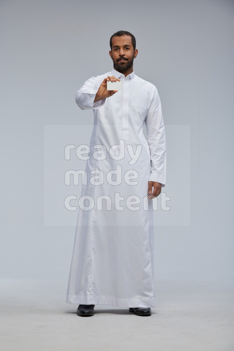 Saudi man wearing Thob standing holding ATM card on Gray background