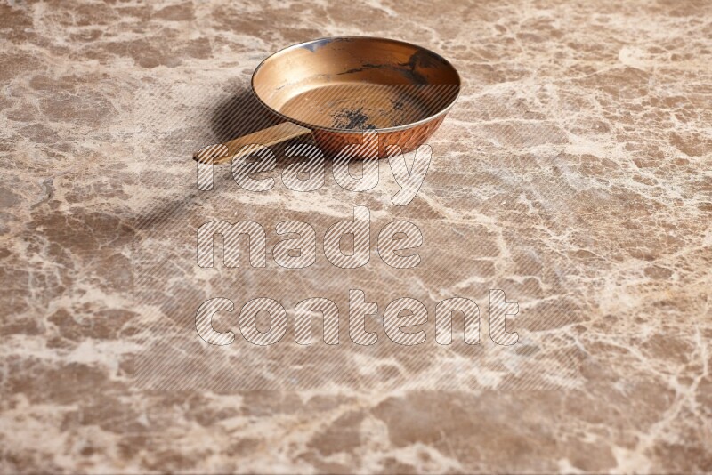 A small copper pan on beige marble background