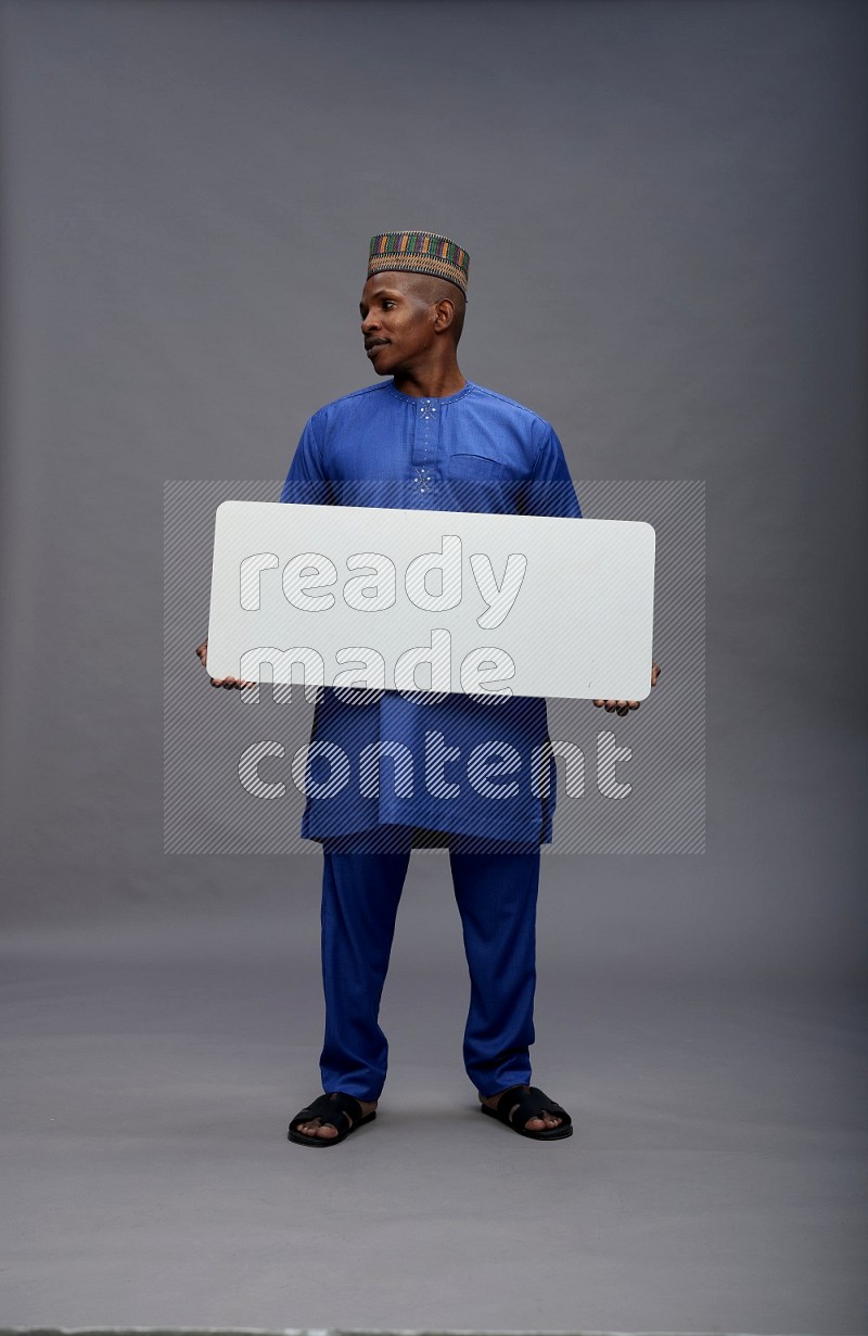 Man wearing Nigerian outfit standing holding board on gray background