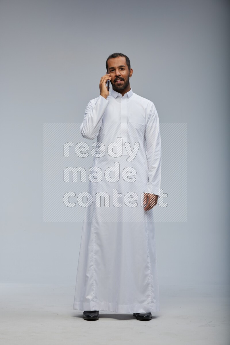 Saudi man wearing Thob standing talking on phone on Gray background