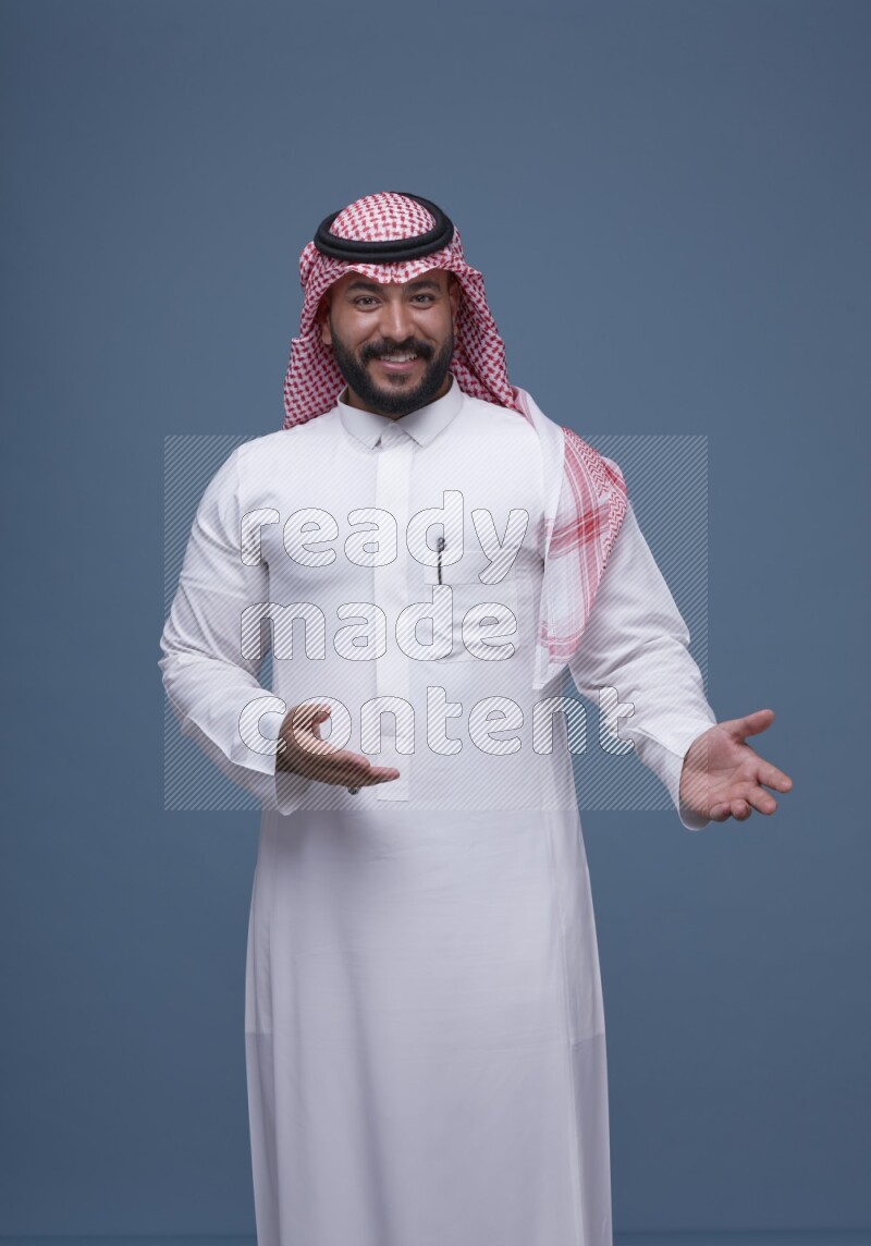A man pointing on blue background wearing Saudi Thob with Shomag