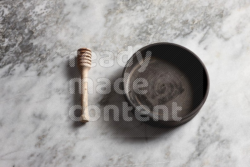 Black Pottery Oven Plate with wooden honey handle on the side with grey marble flooring, 65 degree angle