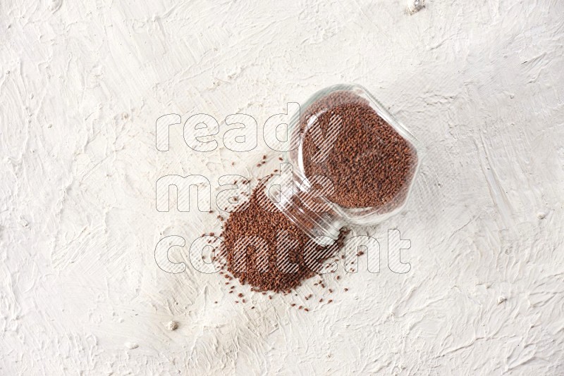 A glass spice jar full of garden cress and jar is flipped with fallen seeds on a textured white flooring in different angles