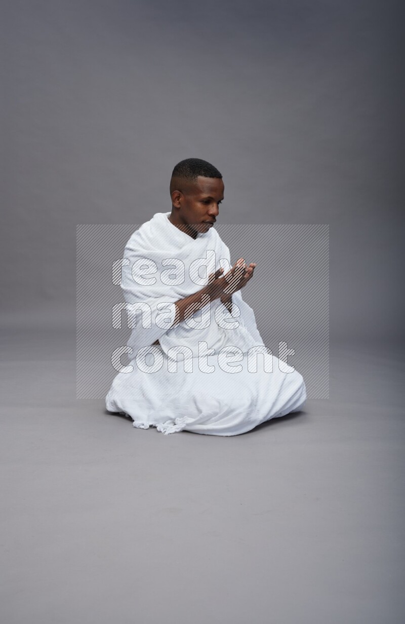 A man wearing Ehram sitting on floor dua'a on gray background