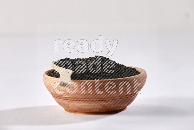 A wooden bowl and wooden spoon full of black seeds on a white flooring in different angles
