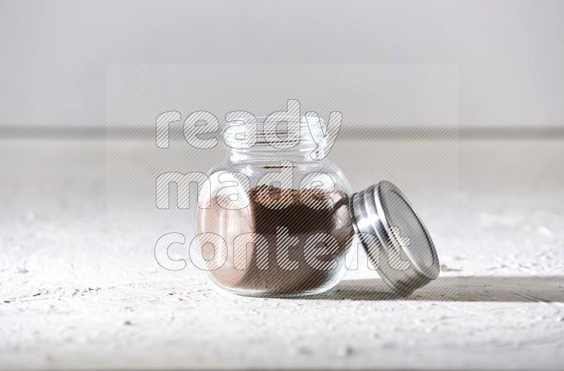 A glass spice jar full of cloves powder on textured white flooring