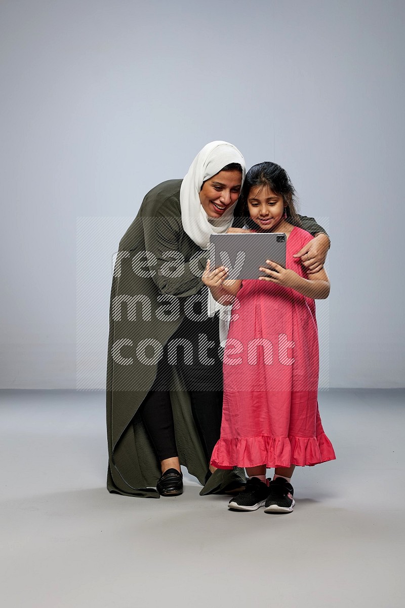 A girl holding an Ipad with her mother on gray background