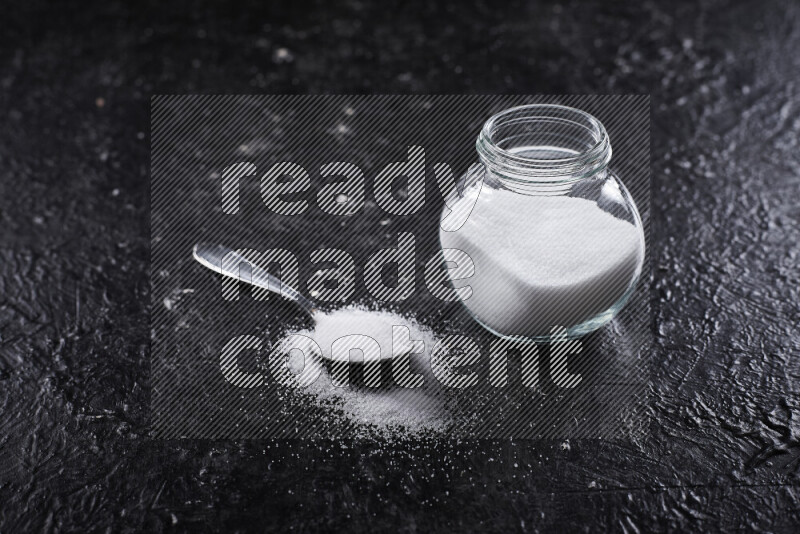 A glass jar full of fine table salt on black background