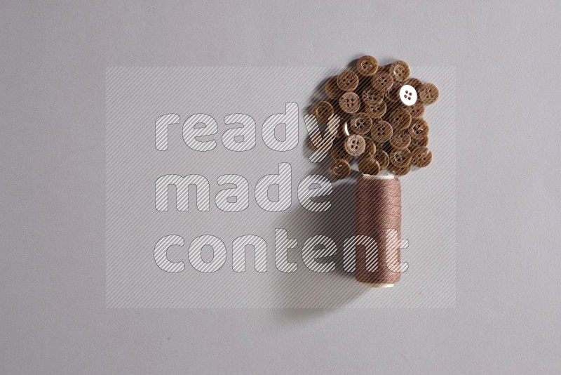 A brown sewing thread spool with colored buttons on grey background