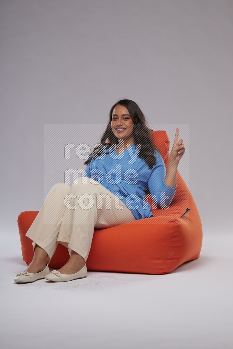 A woman sitting on an orange beanbag and interacting with the camera