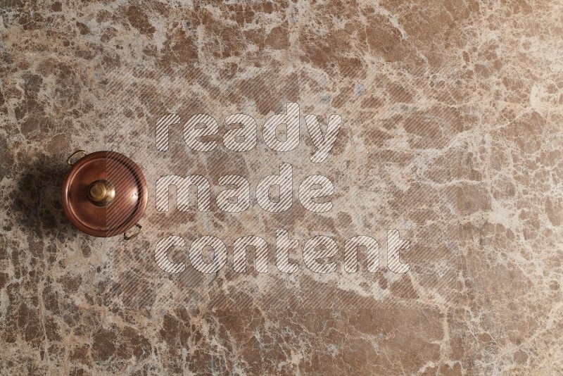 A small copper pot on beige marble background