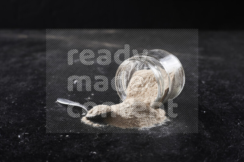 A glass jar full of onion powder flipped with some spilling powder on black background